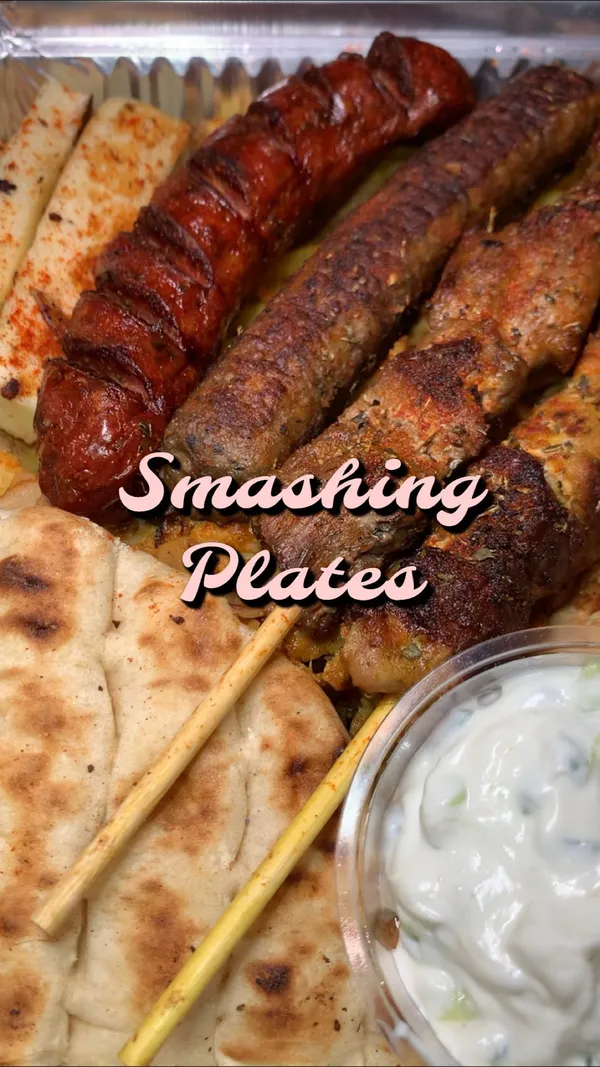 The video showcases a variety of grilled meats, fries, halloumi fries, and a gyro from a takeaway restaurant called "Smashing Plates" in Wembley.  The food is presented in foil containers and on paper. Various dipping sauces are also shown.  The video ends with a baklava dessert.
