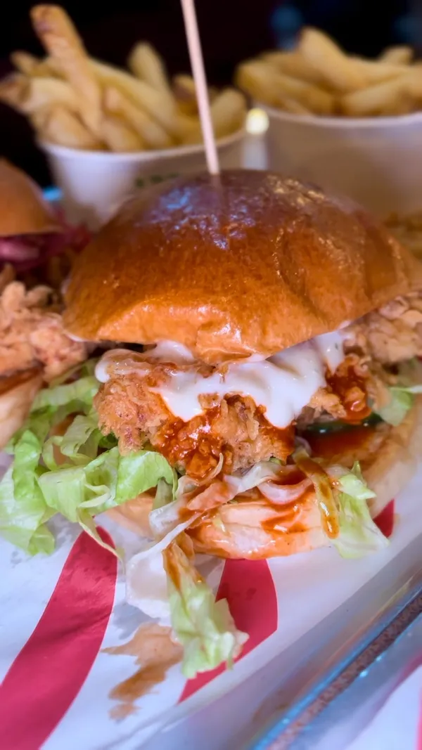 The video showcases a meal from Butchies, a fried chicken restaurant with multiple London locations. It features two fried chicken burgers, fries, and tenders. The burgers are presented in close-up, highlighting the crispy chicken, bacon, and sauce. The fries and tenders are also shown, emphasizing their texture and color. The influencer enthusiastically eats the meal, expressing positive reactions.