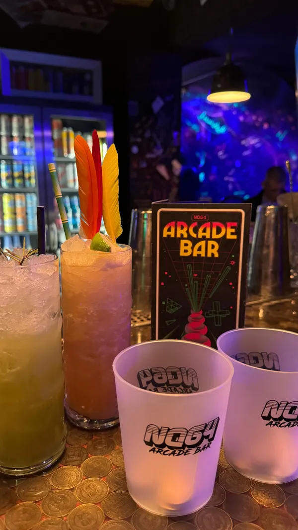 The video showcases NQ64 Arcade Bar, located on Colquitt Street. It features various arcade games, pinball machines, and retro consoles.  The bar offers cocktails, with prices shown as £8.50 for 15 tokens.  The video highlights the vibrant, neon-lit atmosphere of the bar, emphasizing a nostalgic 90s theme.  No specific dietary information is provided.