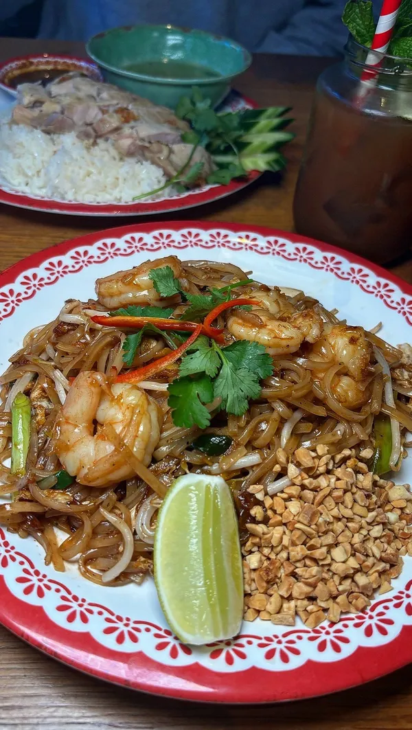 The video showcases a meal at Rosa's Thai in Manchester. It features various dishes, including satay skewers, fried squid, prawn crackers, pad thai, Hainanese chicken rice, and fried banana fritters.  The drinks shown are iced tea and Singha beer.  The presentation emphasizes vibrant colors, close-ups of food textures, and the use of attractive tableware. Dietary information isn't explicitly stated, but the presence of vegetarian options is mentioned in the caption.