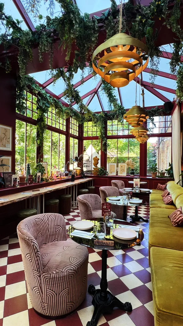 The video showcases the exterior and interior of Eve Kensington restaurant in London, including the lobby, dining area, and garden patio. It features close-ups of a margarita cocktail, chicken wings, a chicken Caesar salad, a Four Cheese pizza, and a New York slice pizza. It shows hands picking up pizza slices and a woman eating a slice. It also shows a cherry being added to a red cocktail.