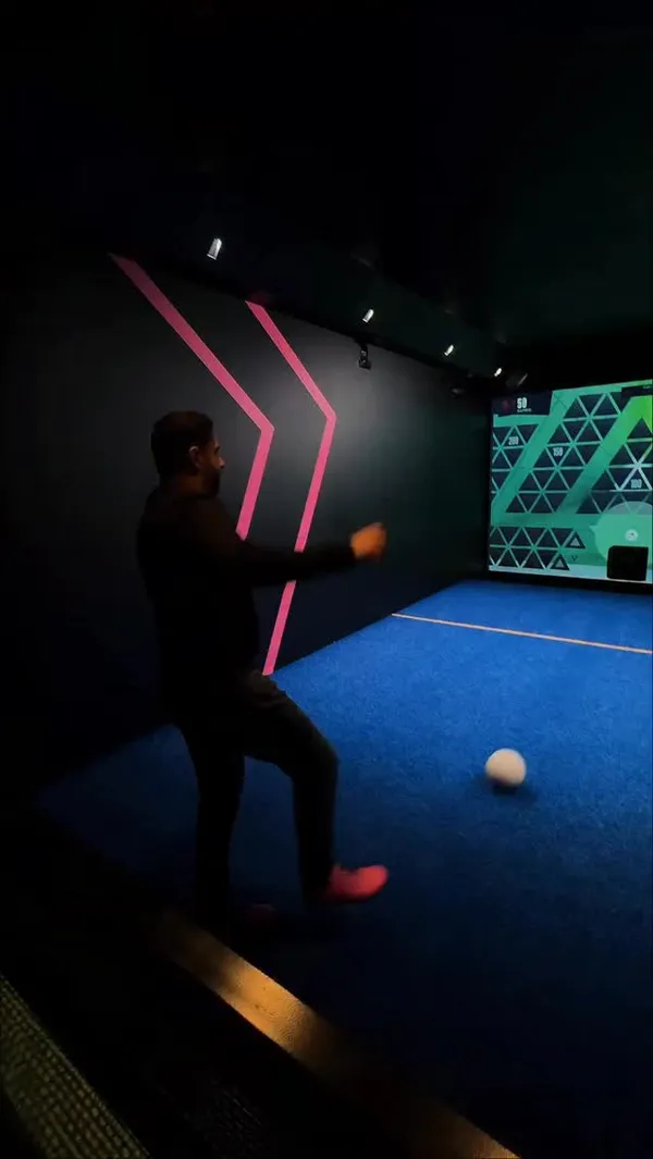 The video promotes TOCA Social, an interactive entertainment venue. It showcases groups of friends participating in digital football games, where they kick a ball at a large screen. The video also features the food and drinks available, including shots of cocktails, chicken wings, a burger with fries, and loaded nachos. The overall atmosphere is portrayed as modern, dark, and energetic, with neon lighting. Other activities like foosball are also briefly shown.