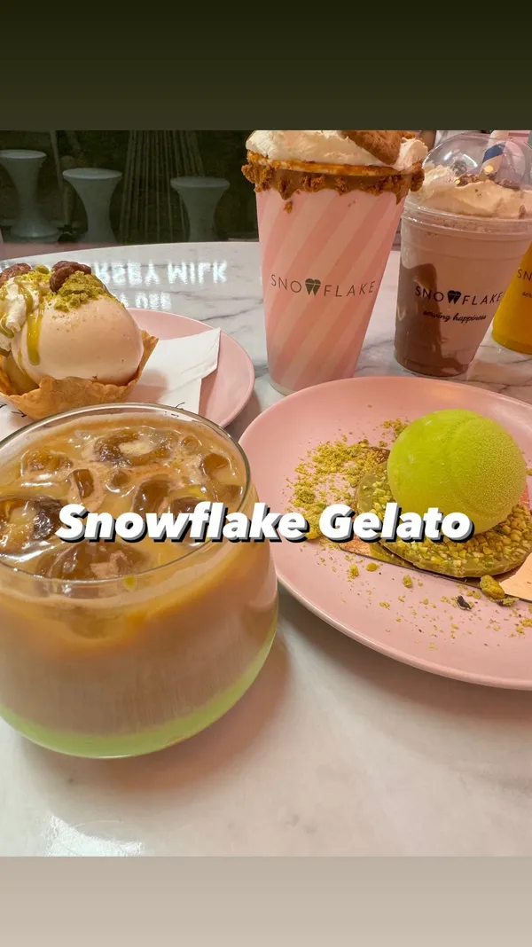 The video showcases Snowflake Gelato in Soho, London. It features various food and drink items including the new "Tennis Ball Dessert" (a pistachio and raspberry mousse dome), a Lotus Biscoff sundae milkshake, an icily gelato bowl, mango granita, a chocolate milkshake, and an iced pistachio latte. The presentation focuses on the visually appealing desserts, with close-up shots highlighting textures and colors.  No specific dietary information is provided.