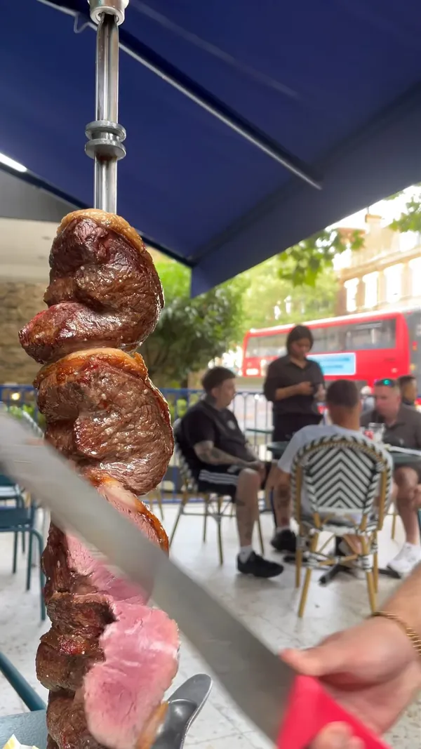 The video showcases Preto Islington, a Brazilian restaurant, offering a weekend brunch.  The buffet features various salads (tomato, cucumber, coleslaw, potato salad), roasted potatoes, French fries, fried polenta, and a selection of sauces. The main focus is on the bottomless meat selection, which includes garlic steak and other cuts, served tableside by servers. The restaurant's ambiance is bright and visually appealing.