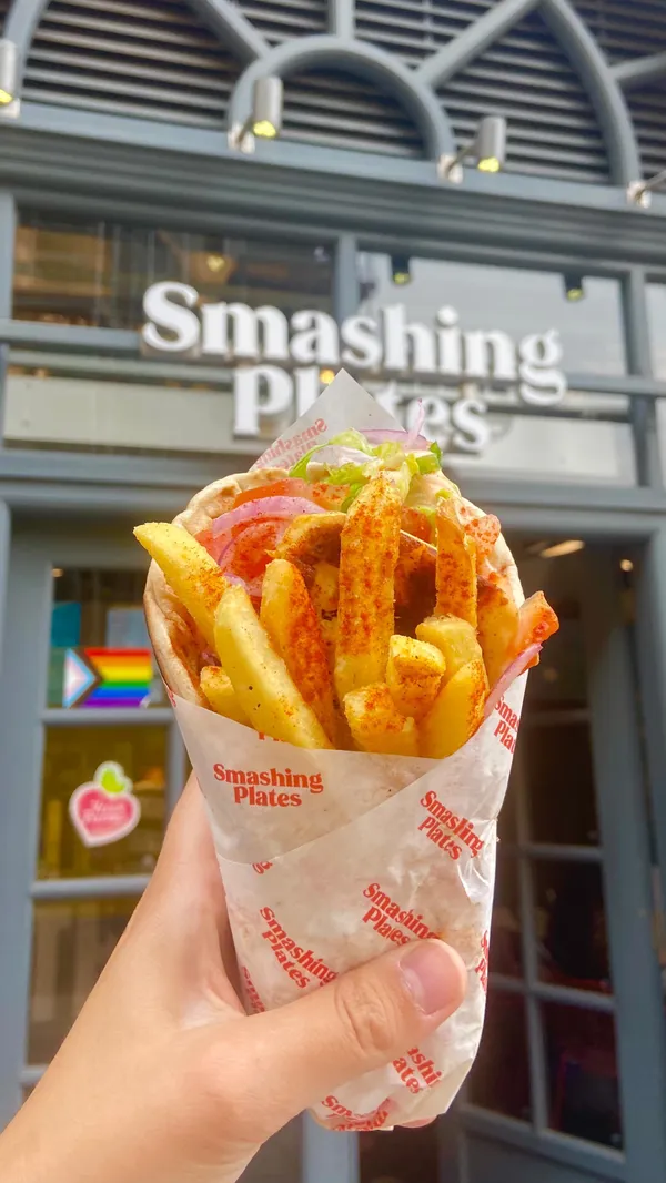 The video showcases Smashing Plates, a Greek street food restaurant located in an archway of London Bridge Station.  It highlights various menu items, including pork and chicken gyros wraps with halloumi and fries, chicken bites with tzatziki, cheesy fries, and pittanuts. The food is presented in visually appealing close-ups and shots that emphasize textures and colors.  The video mentions vegetarian and vegan options are available. The main focus is a vibrant showcase of the food, atmosphere, and branding of Smashing Plates.