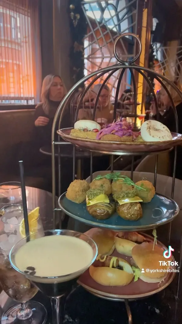 The video showcases a Christmas-themed bottomless brunch at Dirty Martini in Leeds. It features various cocktails (including a Christmas Martini and a White Christmas cocktail), and a selection of food items presented on a three-tiered stand.  These include mini pigs in blankets, turkey sliders, gouda and bacon donuts, flatbreads with hummus, roasted potato hasselback, and truffle mushroom arancini. The food items are presented as bite-sized portions, visually appealing and arranged on plates. No specific dietary information is provided. The primary focus is showcasing the food and drinks while interspersing snippets of a song.