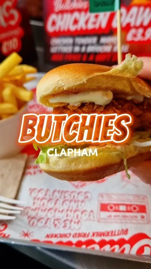 This video reviews a £3.95 chicken dawg from Butchies in Clapham, London. The video shows close-up shots of the sandwich, fries, and a Red Leicester dipping sauce. The reviewer takes a large bite, showcasing the cheese pull, and gives a thumbs-up.