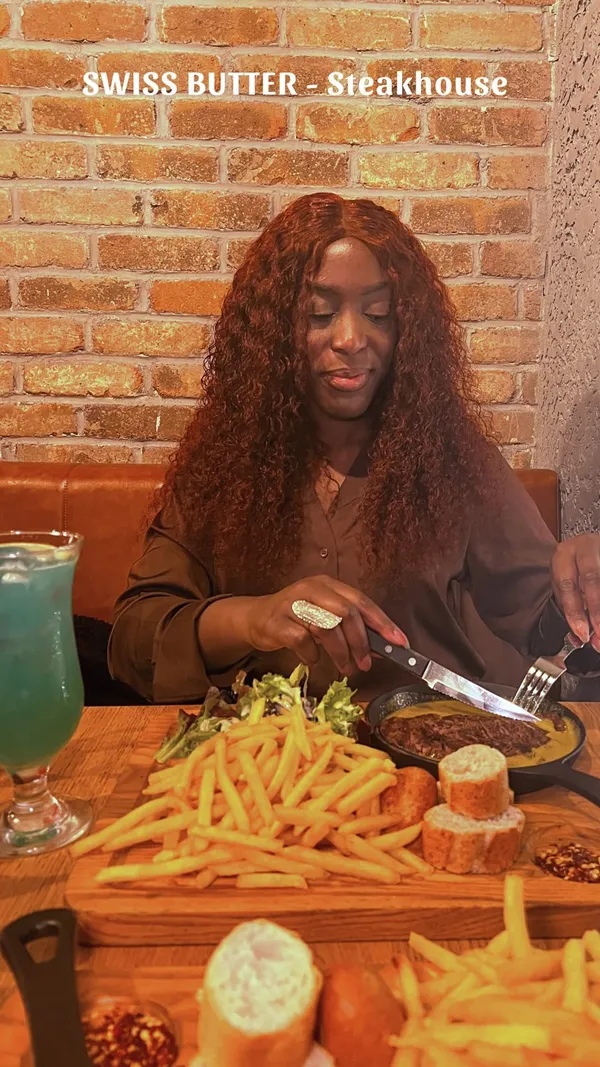 The video showcases a night out at Swiss Butter restaurant in London. It features two cocktails, a beef fillet with Swiss butter sauce, fries and bread, and a molten chocolate lava cake for dessert. The food is presented on wooden platters, with close-ups of the textures and colors of each dish. The video is upbeat and highlights the quality and quantity of the food while also showing the restaurant's ambiance and a brief glimpse of the queue outside. 