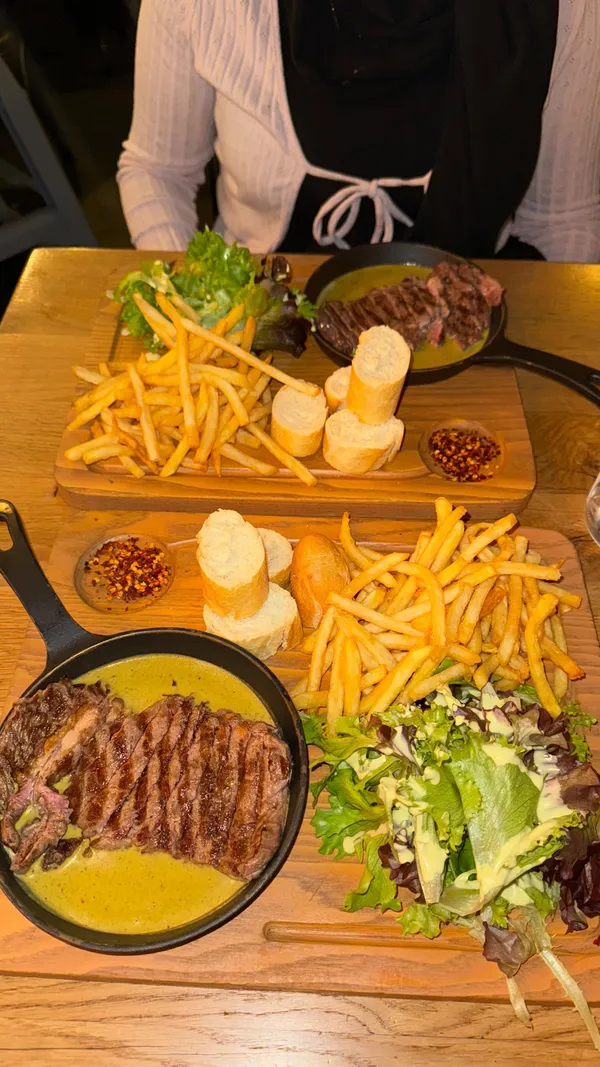 This video showcases a visit to Swiss Butter, a restaurant in London's Holborn. The video features two ribeye steak dishes with fries, salad, baguette, and a green sauce, accompanied by a caramel pain perdu dessert and orange juice. The food is presented on wooden platters, with a focus on close-up shots highlighting textures and colors.  The video emphasizes the deliciousness of the food and the positive dining experience.