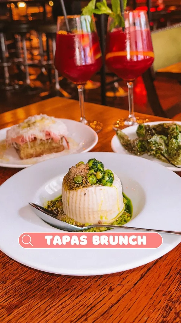The video showcases a tapas brunch at Ember Yard restaurant in Soho, London.  It features various tapas dishes, including padron peppers, focaccia with mortadella and manchego, pan-fried prawns with croquettes, grilled chorizo with pineapple, burrata with pea pesto, and tortilla Española.  Two types of sangria and prosecco are also shown. The dishes are presented attractively on white plates against a wooden table. The video ends with churros and chocolate sauce. The overall focus is on the food and drink offered in the tapas brunch.