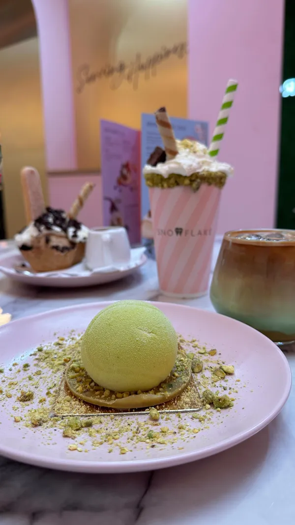 The video showcases Snowflake Gelato, a cafe offering various summer treats. It features a pistachio gelato dessert ('tennis ball' themed), coffee, and strawberry-themed drinks. The food presentation emphasizes pastel colors and visually appealing arrangements. No specific dietary information is provided. The main focus is presenting the cafe's summer menu items.