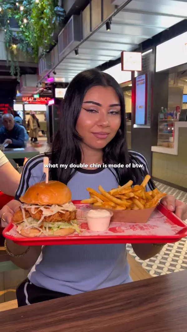 A short, fast-paced video showcasing a meal from Butchies, a buttermilk fried chicken restaurant located in a food hall. The video features an influencer presenting a tray with a chicken burger and fries. It includes close-up shots of sauce being poured on the burger, fries being dipped into a sauce, the influencer taking a bite, and a final shot of the menu. The main items shown are the 'Pineapple Express' chicken burger and 'The Original' burger, along with seasoned fries and gravy.