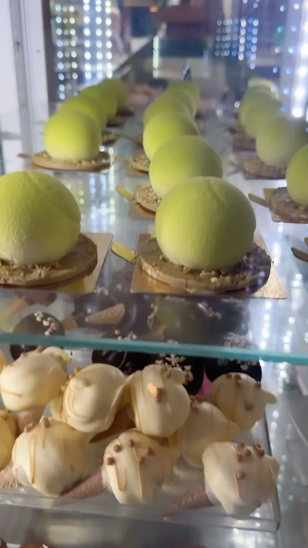 The video showcases Snowflake Gelato, a cafe, featuring their Wimbledon-themed limited edition desserts and summer menu items. These include a 'snowball' dessert resembling a tennis ball (strawberry compote, vanilla, and pistachio), mini pistachio and salted caramel white chocolate cones, and a lotus biscuit milk cake. The video uses close-up shots to highlight the textures and colors of the desserts.