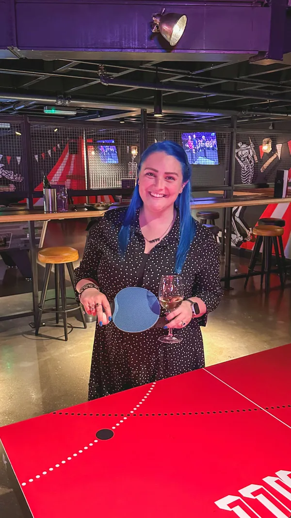 The video showcases Bat and Ball, a bar in Westfield Stratford, London. It highlights the food menu (pizzas, burgers, chicken wings, etc.), the wine list, and the game area upstairs with ping pong, pool, darts, and karaoke. The food presentation focuses on variety and sharing platters. Dietary information isn't explicitly shown. The primary focus is on the overall experience at the bar.