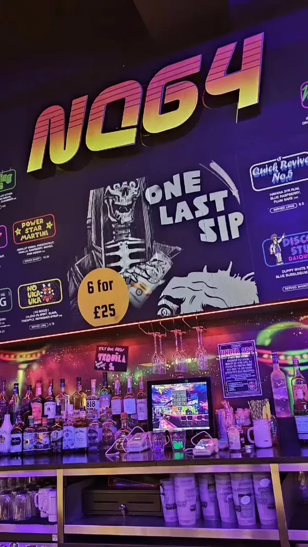 The video showcases NQ64, a bar with retro arcade games. It features cocktails being prepared (one flambéed), patrons playing games, and shots of the bar's atmosphere.  The cocktails shown include a mason jar drink with a frothy top and a martini-style drink.
