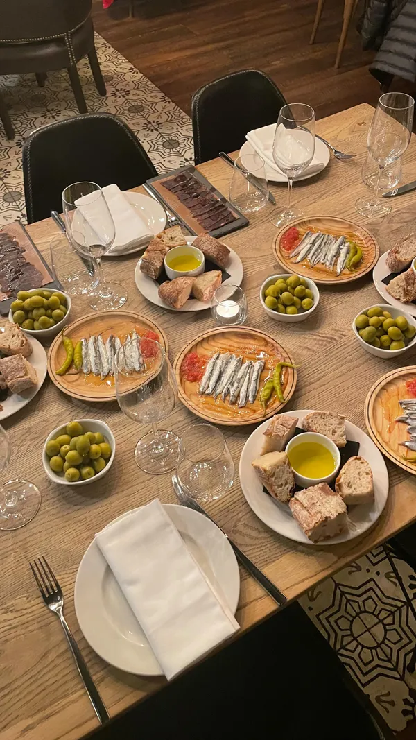 The video showcases a festive tapas dinner at Iberica Restaurants.  It features various tapas dishes, including cheese platters, olives, anchovies, jamon (cured ham), croquettes, black rice with prawns, and churros with chocolate sauce. The presentation is elegant, with the food arranged attractively on wooden boards and plates. The setting is a dimly lit, upscale restaurant with a festive atmosphere. The primary focus is the meal itself and the ambiance.