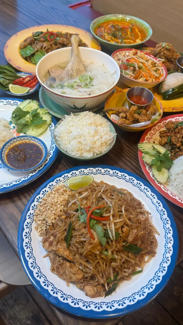 The video showcases Rosa's Thai restaurant. It features a passion fruit and jasmine bubble tea, and various Thai dishes including Pad Thai, chicken wings, beef massaman, drunken noodles, noodle clear broth, and others. The food is presented on colorful plates and bowls. The main focus is on the meal showcase, highlighting the taste and variety of the food.