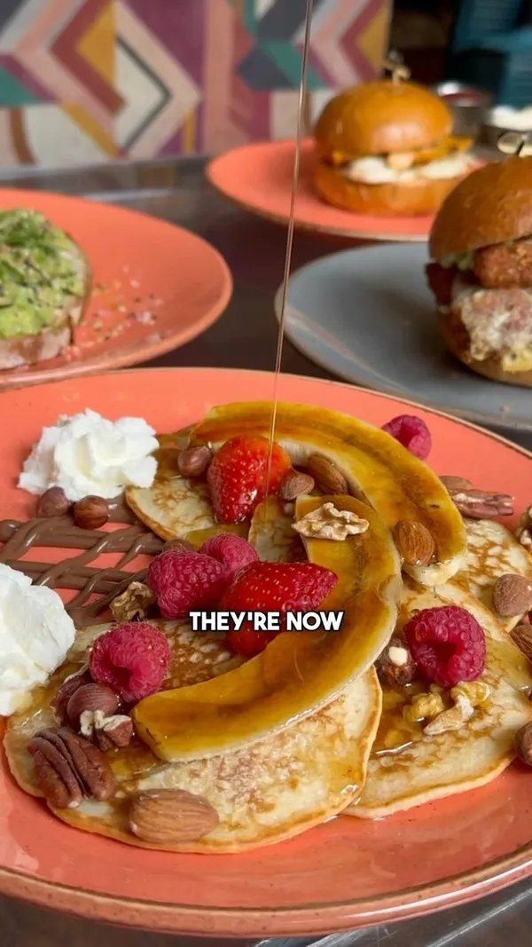 This video showcases a bottomless brunch experience at The Little Yellow Door, a bar in Notting Hill, London, that also serves brunch on weekends. The video highlights various brunch items: avocado toast, chicken burger, halloumi burger, pancake stack with banana and berries, and a vegan pesto toastie.  The food is presented in a visually appealing manner, with close-ups and overhead shots. Dietary options such as vegan choices are included. The main focus is showcasing the food and the overall brunch experience. 