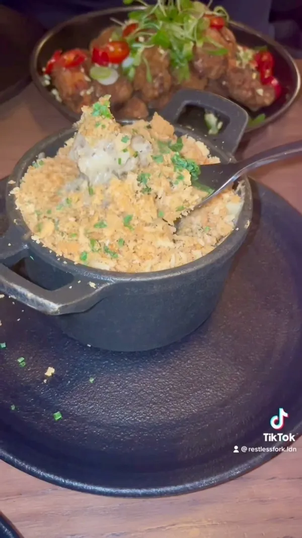 The video showcases a meal at Wingmans in Soho, London. It features a yellow cocktail, various chicken wing dishes (including Szechuan and Hoisin duck wings), pork belly bites, and truffle mac and cheese.  The food is presented on dark plates and in small, cast-iron dishes.  The video shows preparation of dishes in the kitchen and shots of the restaurant's ambiance. Gloves are provided with the saucy wings.