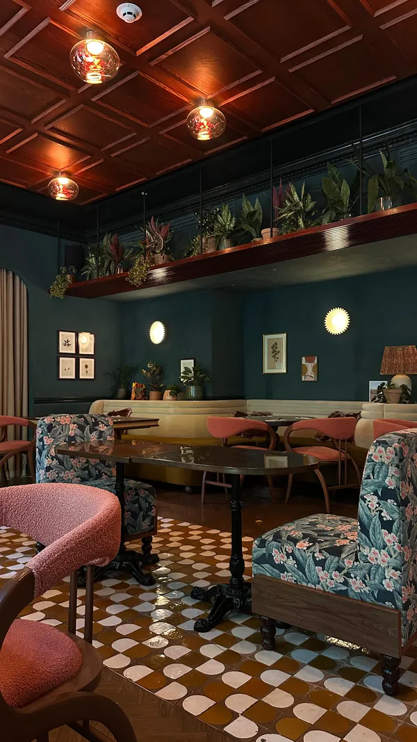 The video showcases a restaurant interior with stylish decor and seating areas. It features close-ups of a large pizza with pepperoni, cheese, and basil, and a glass of orange cocktail with ice and a straw. The video concludes with two women smiling and toasting with their cocktails.