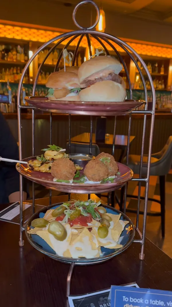 The video showcases a bottomless brunch experience at Dirty Martini, a bar in London.  The food is presented on a three-tiered serving stand, resembling a birdcage. Items include beef and cheese sliders, battered fish sliders, grilled chicken skewers, crispy truffle mushroom arancini, and nachos.  Various cocktails are also featured, notably martinis with different garnishes. The primary focus is on the food and drink offerings, emphasizing the quantity and visual appeal of a bottomless brunch.