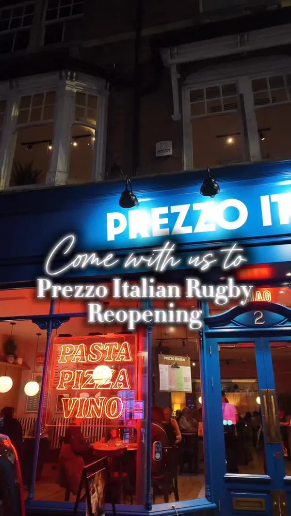 The video promotes the reopening of the Prezzo Italian restaurant in Rugby. It starts with an exterior night shot of the restaurant, then moves inside to display the modern decor, including neon signs and striped booths. The content showcases a variety of cocktails and dishes, such as fried appetizers with a dipping sauce, ravioli and penne pasta being topped with freshly grated parmesan, a baked lasagna-style dish, seasoned fries, and flatbreads. The video concludes with a shot of a chocolate dessert topped with ice cream and sauce.