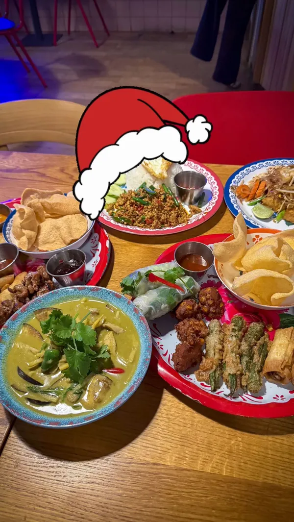 The video showcases a Thai feast menu at Rosa's Thai restaurant. It features various dishes including starters like a classic platter with Thai fried chicken, veggie spring rolls, pork skewers, calamari, and prawn crackers; a veggie platter with fresh summer rolls, sweetcorn fritters, okra tempura, veggie spring rolls, and pumpkin crackers; main courses such as green curry, Pad Thai, and Massaman beef curry; and dessert, Thai churros. The food is presented on colorful plates in a casual restaurant setting. Dietary options for vegetarians are clearly shown. The main focus is on showcasing the variety of dishes and their appealing presentation.