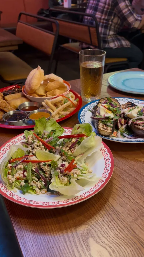 The video showcases the Songkran Family Feast menu at Rosa's Thai restaurant. It features various dishes including a sharing platter with grilled pork skewers, Thai fried chicken, larb gai (spicy chicken in lettuce wraps), and yum makhuea (grilled aubergine salad). Main courses shown are chicken pad Thai and khao man gai (chicken with rice). Desserts include mango sticky rice and Thai churros with condensed milk. The video highlights the £30 per person price for the 3-course menu.