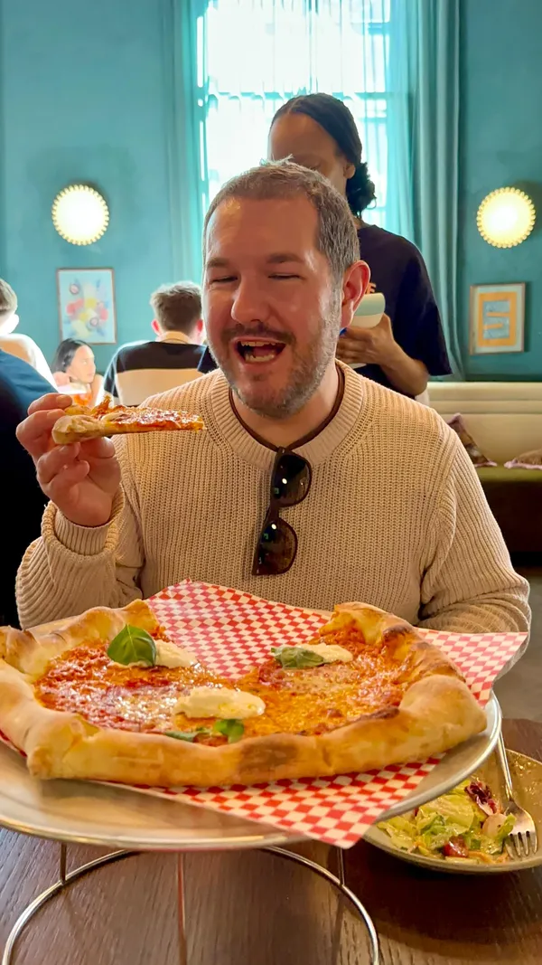 The video promotes an unlimited pizza brunch at Eve X Proper Slice, located in a hotel near Earls Court, London. It features close-ups of various pizzas, including pepperoni and a vegetable-topped pizza, a side salad, and a cocktail. The video emphasizes the unlimited pizza offer for £20 per person for 90 minutes and highlights that selected cocktails are available for £5. It shows individuals enjoying the pizza and provides glimpses of the venue's exterior and interior.