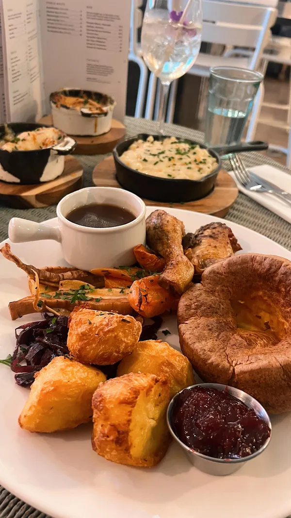 The video showcases a Sunday roast at No.1A Duke Street in Richmond.  It features various dishes including crispy squid, aubergine and chickpea dip with flatbread, roast chicken with cranberry sauce, pork belly with apple sauce, roast potatoes, Yorkshire puddings, cauliflower cheese, and a caramelized lemon tart.  The drinks shown include cocktails like Elderflower Spritz and a mango and coconut margarita. The restaurant's interior is also briefly shown.