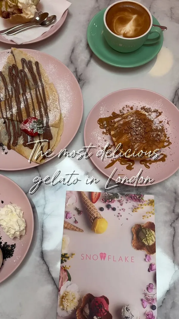 The video showcases Snowflake Gelato in Soho, London. It features various desserts, including crepes with chocolate sauce and ice cream, a chocolate molten cake with ice cream and cream, an ice cream dessert in a waffle bowl, and a unique Wimbledon tennis ball-shaped dessert. The desserts are presented on pink plates against a marble table. The cafe's interior is also shown, with pink walls and marble tables. The video focuses on the visual appeal of the desserts and the cafe's aesthetic.