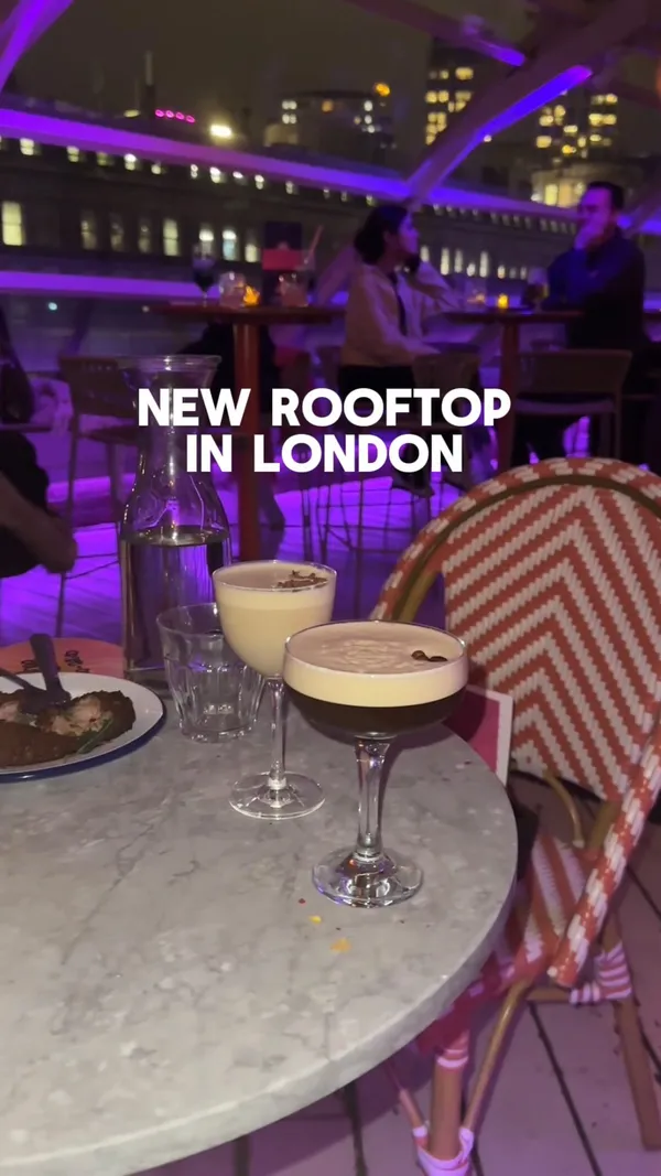 The video showcases a new rooftop bar in London, featuring cocktails and small plates.  The setting is a trendy, dimly lit rooftop space with city views. Food items shown include fried chicken, corn on the cob, and what appears to be calamari. Drinks include two cocktails, one appearing to be a creamy, possibly espresso martini-style drink. The presentation focuses on the atmosphere and the food's visual appeal, with a focus on color contrast and plating.
