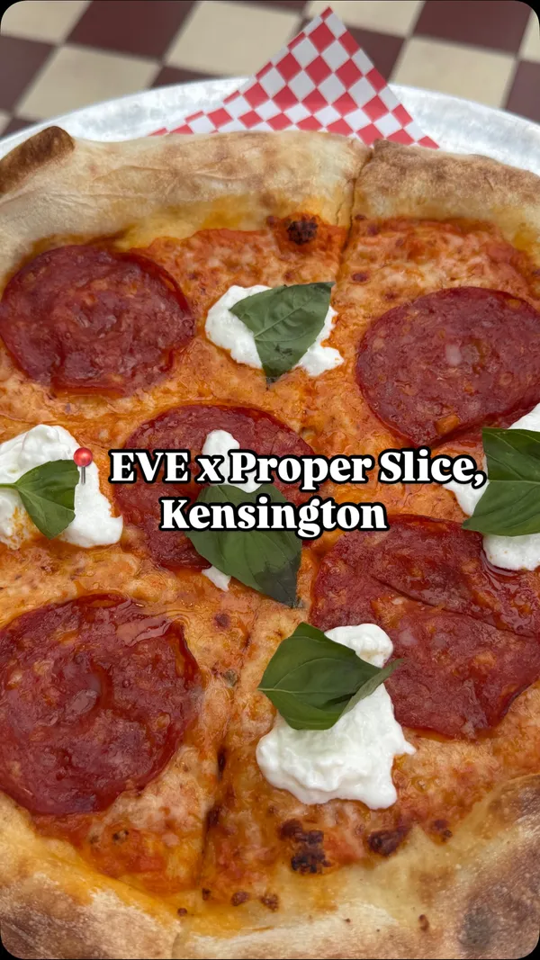 The video showcases the EVE x Proper Slice restaurant in Kensington. It features the exterior of the building, followed by interior shots of the dining area, including tables set with menus and glassware, a green velvet sofa, and the bar area. The video then highlights specific food and drink items: an Aperol spritz, a Brooklyn Lager beer, a pizza topped with pepperoni, basil, and dollops of cheese, another pizza with artichokes, olives, and jalapenos, and a plate of garlic knots with marinara sauce. The main focus is on presenting the restaurant's ambiance and the variety of food and drink options available.