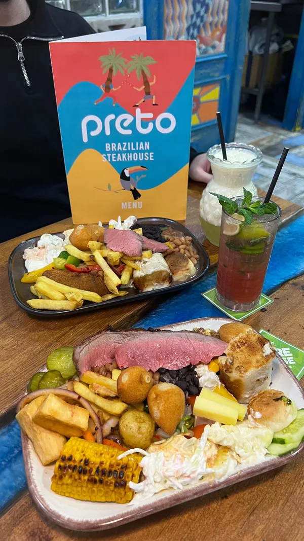 This video promotes Preto, a Brazilian Rodizio restaurant in the West End. The video showcases the unlimited Brazilian BBQ experience, featuring various cuts of meat such as lamb, beef, chicken wings, ribs, and Brazilian sausages, all carved in front of the customer. It also highlights the unlimited buffet with traditional dishes like Feijoada, Coxhinhas, and Pao de Quejo, along with salads and dips. The video also shows desserts like Brigadeiro, chocolate cake and flan. Drinks are also shown. The main focus is on the unlimited Rodizio grill and the variety of food offered.