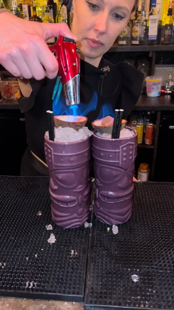 The video showcases the Tequila Mockingbird bar in London, highlighting their 2-for-1 happy hour cocktail deal. It features two bartenders expertly preparing cocktails, including a flaming one, and also shows a creamy alcoholic coffee drink. The bar's atmosphere is vibrant and energetic, with warm lighting and a lively ambiance. The focus is on the drinks, their preparation, and the happy hour promotion.