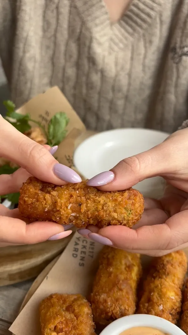This video showcases a Sunday roast meal at 197 Chiswick Fire Station.  It begins with a close-up of Nduja and Cheddar croquettes being pulled apart, showing the cheese pull.  Then it shows dipping a croquette in sauce. Next, it shows a passionfruit drink, followed by several plates of roast dinners with various meats (beef, chicken, pork), roast potatoes, Yorkshire puddings, gravy, and vegetables. Finally, it shows an apple and raspberry crumble with ice cream and a mango sorbet. The food is presented attractively, and the setting appears to be a modern, upscale restaurant.