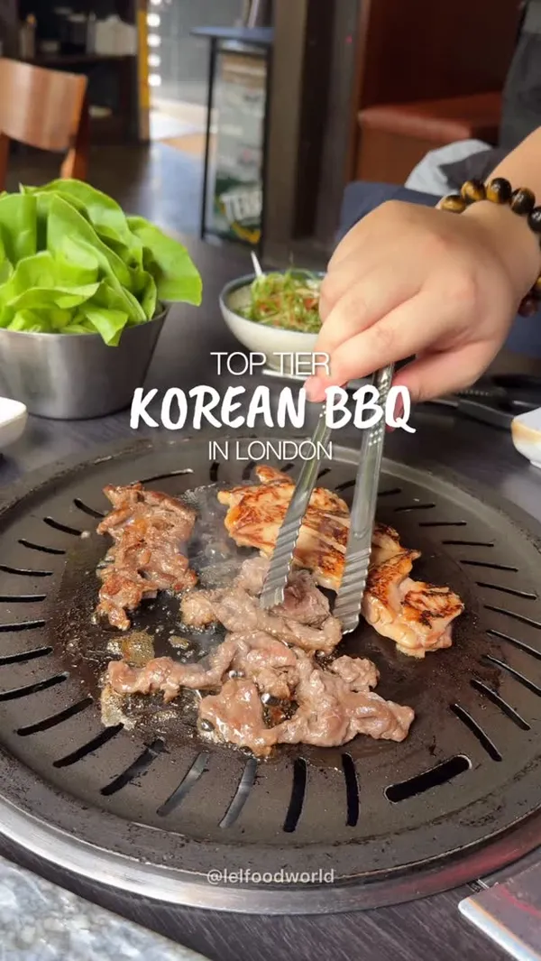 A fast-paced video showcasing the Korean BBQ experience at Gogi restaurant in London. The video features close-up shots of various meats, including beef and chicken, sizzling on a tabletop grill. It also highlights other dishes such as a platter of raw marinated meats, braised beef short ribs (galbijjim), and a Korean pancake (pajeon). The video shows the interactive element of the meal, with someone using tongs to cook the meat and another person preparing a lettuce wrap. The video concludes with text overlay providing the restaurant's name and address, followed by a brief shot of the restaurant's exterior.