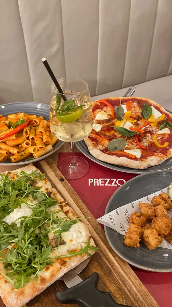 The video showcases a meal at Prezzo, an Italian restaurant. It features various dishes including pizzas (mushroom, burrata, and truffle; another with peppers), pasta (arrabbiata), fried mozzarella balls with a green sauce, cannelloni, affogato, and lemon meringue pie. The presentation is appealing with overhead shots of the pizzas, close-ups of individual dishes, and clear shots of drinks and desserts.  No specific dietary information is provided.