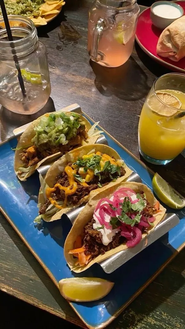 The video showcases a bottomless brunch event at Barrio Angel, a bar in London.  It features various cocktails (including margaritas and champagne), tacos, nachos, and live entertainment including a 90s hip hop bingo game. The food is presented in typical bar food style, nothing particularly noteworthy in presentation; nachos and tacos are in red plastic baskets. The video focuses on the fun atmosphere and the overall experience of the bottomless brunch, highlighting the value for money.
