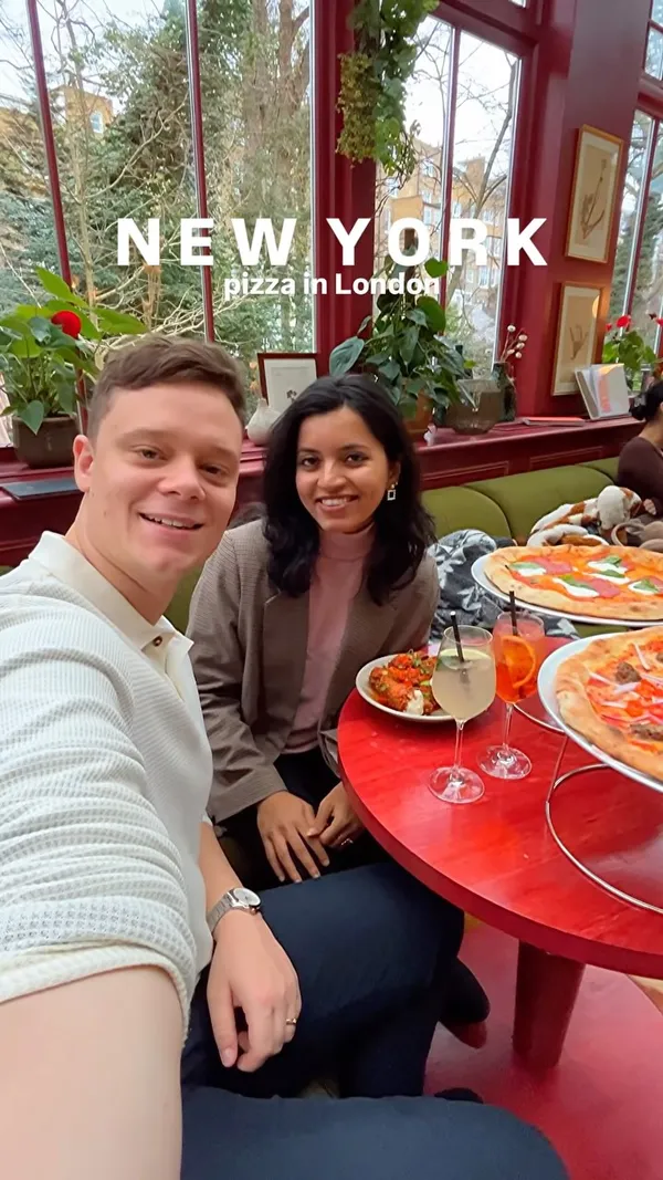The video showcases Eve, a restaurant in Kensington, London, promoting its New York-style pizza and other menu items. The video opens with a couple toasting drinks in a brightly lit, plant-filled setting. It then transitions to a close-up of a pepperoni pizza with basil and mozzarella, followed by shots of the couple enjoying their meal, including fried chicken with chili and spring onion garnish, and two different pizzas (one pepperoni, one with red onion and chili). The video also features interior shots of the restaurant, highlighting its decor and ambiance.