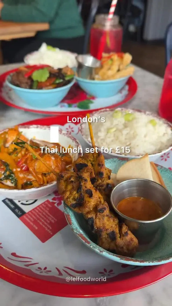 The video promotes a £15 Thai lunch set at Rosa's Thai. It showcases various dishes served on colourful trays, including chicken satay skewers with dipping sauce, fried calamari being squeezed with lime, a stir-fry, and a curry, all accompanied by rice. The deal also includes two red sodas in mason jars. The video ends with a brief shot of the restaurant's interior, featuring red booths and wooden decor.