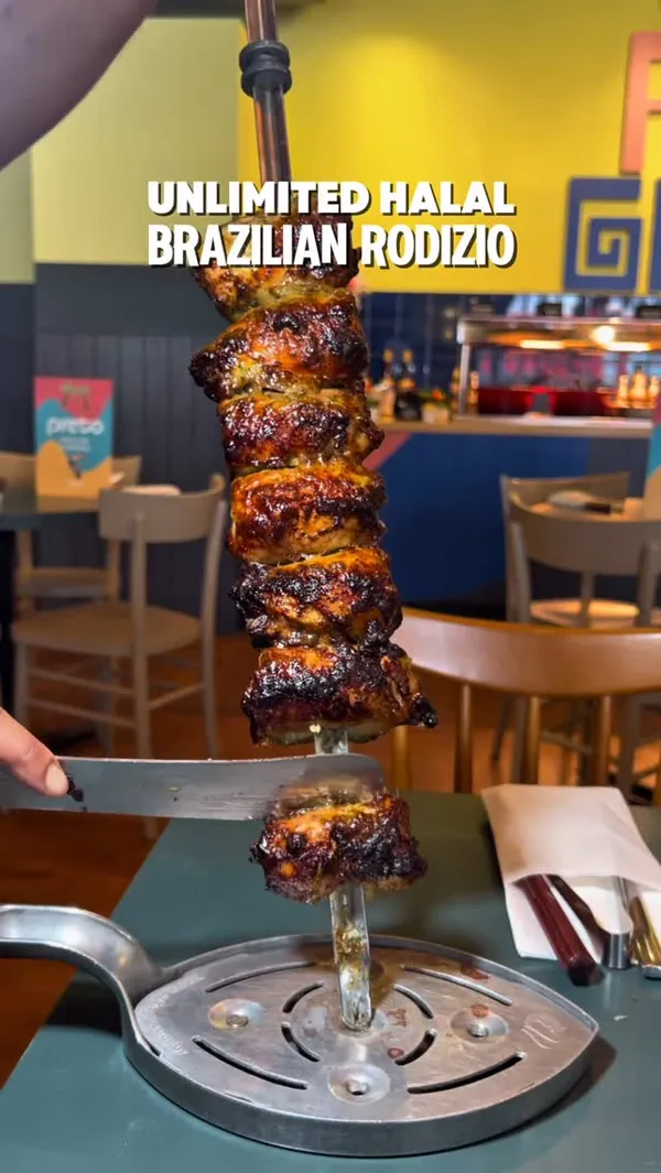 The video showcases a Brazilian steakhouse experience. It features a table setting with various sides like pasta salad, potato salad, and fried cassava, along with cocktails. It highlights the unlimited Rodizio grill concept with servers carving meat directly at the table, including chicken and beef. The video also shows a large buffet spread with salads (tomato, sweet corn, cucumber, beetroot & orange, pasta salad, potato salad) and hot dishes (fried polenta, pan-fried vegetables, white rice, mixed rice). Desserts like cheesecake and flan are shown. The interior and exterior of the restaurant are also briefly featured.