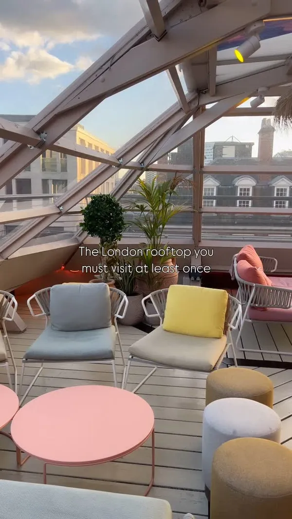 The video showcases a rooftop venue in London, highlighting its ambiance, food, and drinks. It features shots of the seating areas with views of the city skyline, a table displaying several small plates including what appears to be hummus with pita bread, a salad with chicken, and a dish with sweet potatoes. The video also shows a photo booth and a close-up of a cocktail.