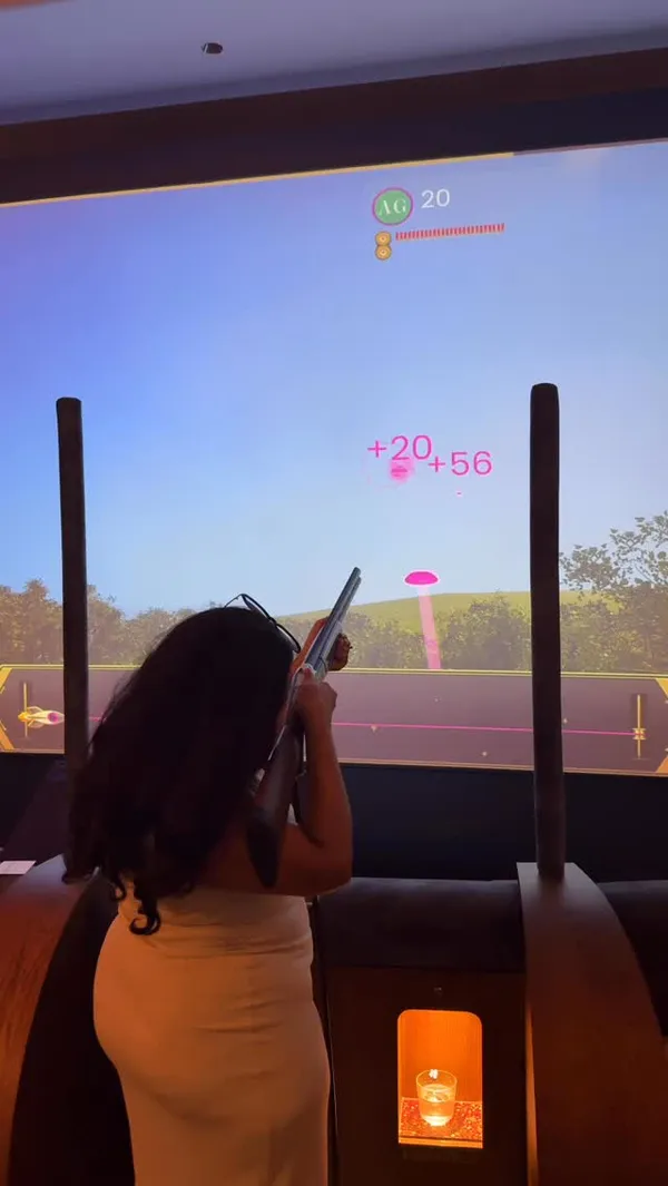 A couple visits Clays, a venue in London offering virtual clay pigeon shooting, showcasing the gameplay, the bar area, and the cocktails.