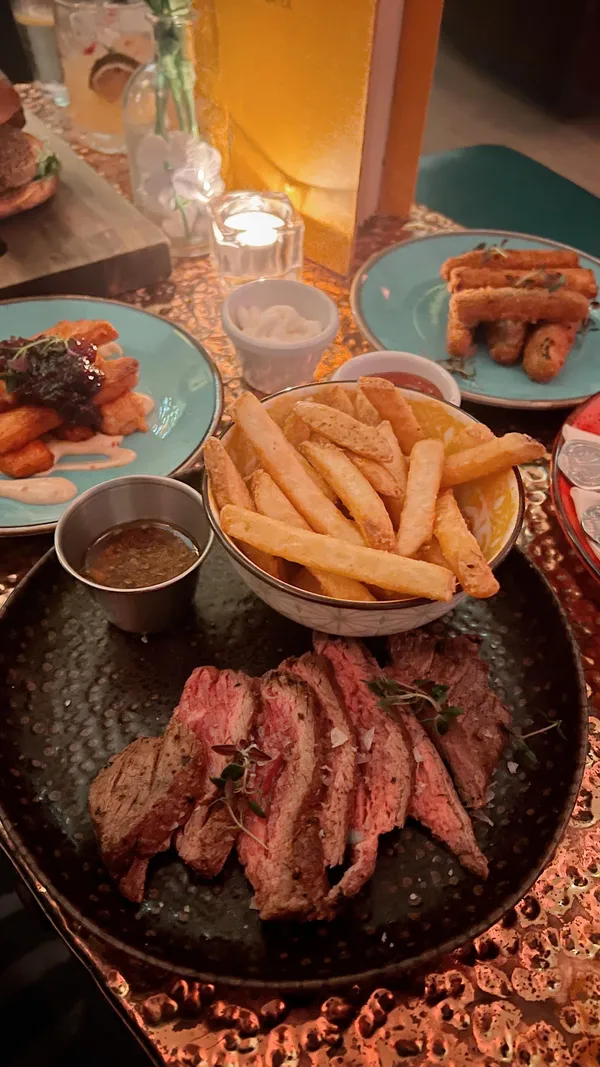 The video showcases The Little Blue Door, a bar in Fulham Road, London. It highlights their cocktails (Tommy's Margarita and Picante), food (vegetarian burger with fries, various small plates, and a steak and chips special), and the bar's interior design.  The presentation is vibrant, showcasing a mix of colorful decorations and the food in various angles.  The video doesn't explicitly mention any dietary restrictions but shows vegetarian options. The main focus is on the overall dining and drinking experience at the establishment.