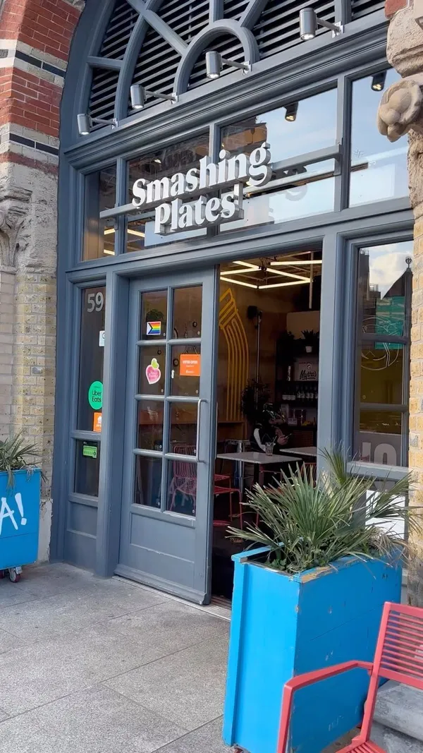 The video showcases Smashing Plates, a Greek restaurant in London Bridge. It presents various food items including gyros (meat wraps with fries), seasoned fries, fried cheese triangles, and baklava. The food is presented in cardboard boxes and wrapped in branded paper. The video is primarily focused on showcasing the food.