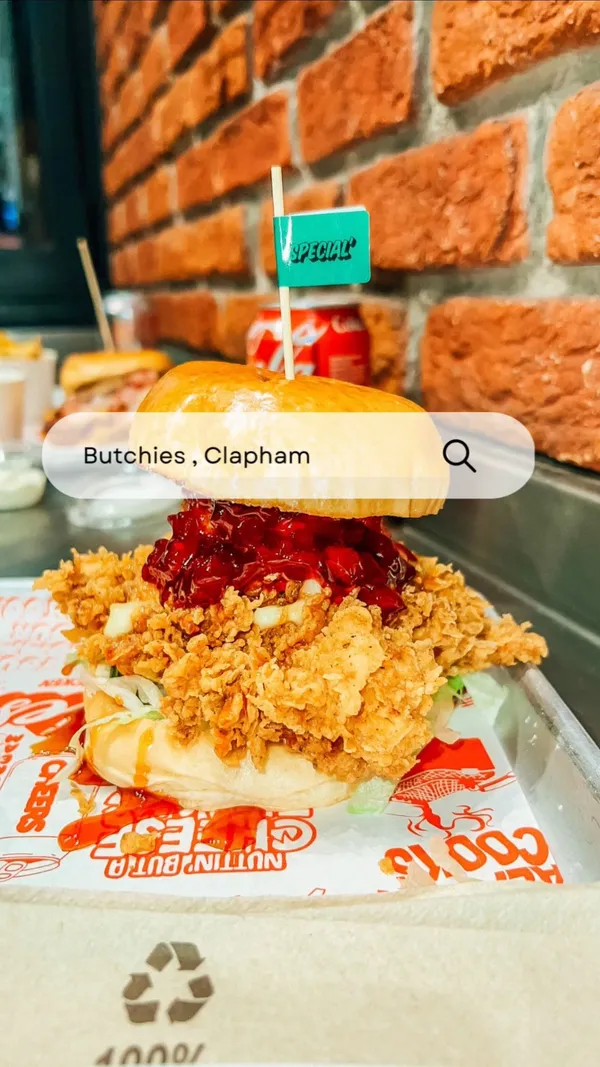 The video showcases Butchies, a restaurant in Clapham, London, promoting their Christmas special burger, the "Sweet Baby Cheesus."  The burger features buttermilk chicken tenders, deep-fried Camembert, cranberry sauce, chili honey, and pickles.  The video also highlights their mac and cheese and cheese-loaded spicy fries.  The food is presented in various shots, focusing on close-ups to highlight textures and appetizing visuals.  A person happily eating the burger is shown. 50p from each burger sold is donated to a local soup kitchen. 