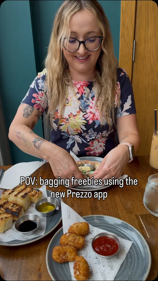 A promotional video for the restaurant chain Prezzo, focusing on a special offer for free Nutella doughnut balls available through their app. The video showcases various dishes including mac and cheese croquettes, a black pepper and mozzarella dough twist, grilled bread with dips, a salmon and prawn creamy pasta, and a large cheeseburger with fries. It shows the food being served and eaten, as well as the restaurant's exterior and interior, and explains how to claim the offer via the app.