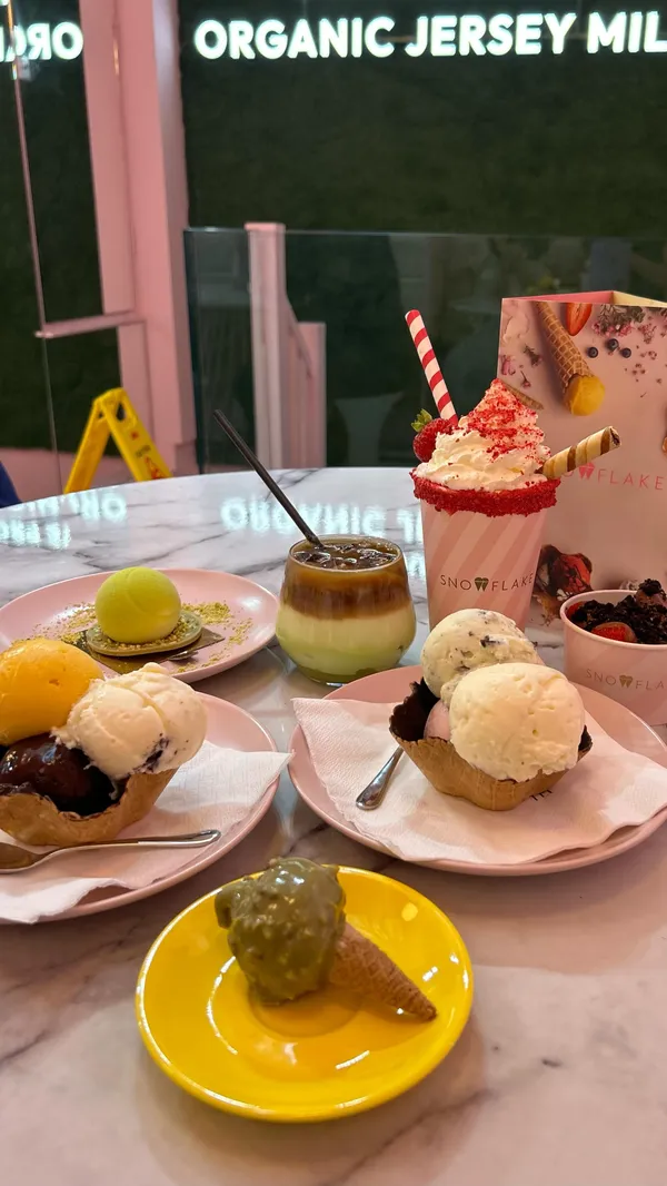 The video showcases Snowflake Gelato, a cafe in London. It features various desserts, including ice cream in waffle bowls, a milkshake, a coffee-based drink, and chocolate-covered strawberries. The presentation emphasizes a clean, aesthetically pleasing style with pastel colors and a focus on visual appeal. No specific dietary information is given. The primary focus is showcasing the desserts and the cafe's ambiance.