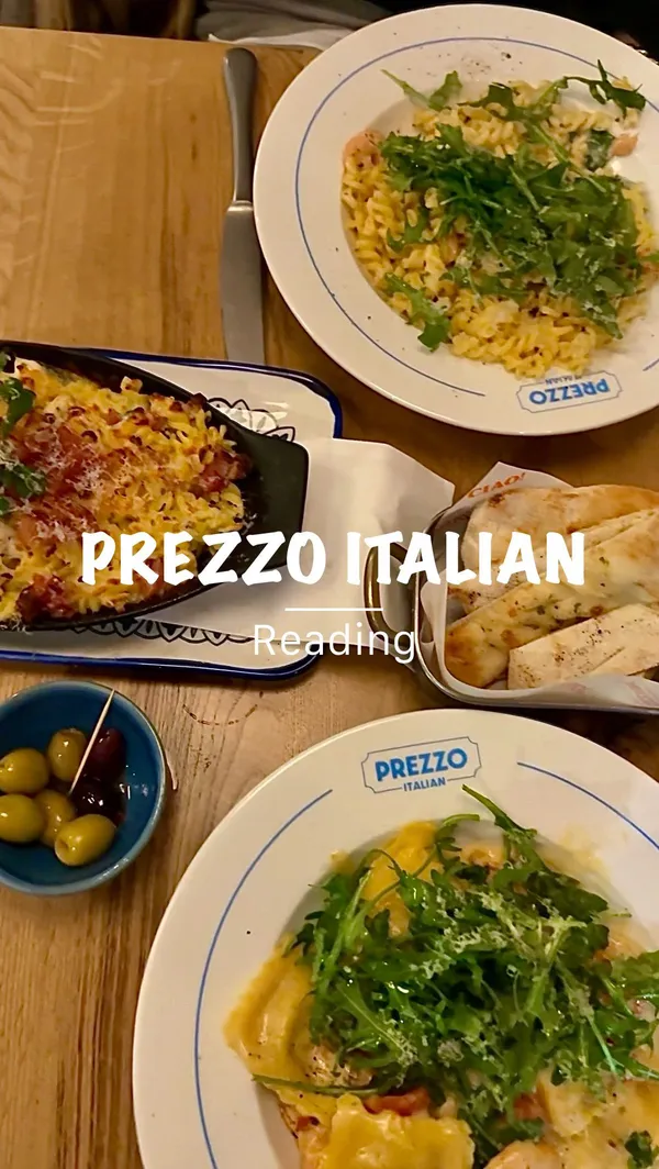 The video showcases a dining experience at Prezzo Italian restaurant in Reading. It begins with exterior shots of the restaurant, then moves inside to show the decor and ambiance. The video features a server pouring prosecco, followed by a montage of various dishes. These include hot honey glazed mozzarella sticks with a prominent cheese pull, gluten-free garlic bread, crab and lobster ravioli, chicken spaghetti carbonara (al forno), chicken mushroom garlic pasta, an affogato dessert with espresso being poured over ice cream, Nutella doughballs being dipped in chocolate sauce, and a final toast with small bottles of Pallini Limoncello. The video concludes with a night shot of the restaurant's exterior.
